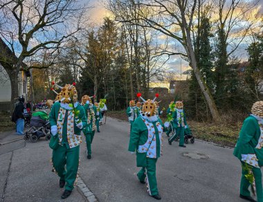 Nussdorf, Uberlingen, Almanya - 11 Ocak 2025. Geleneksel karnaval alayı yıllık Fasnet, Fasnacht veya Fasching festivalinde. Yeşil kostümlü ve maskeli bir grup Nussdorf salyangozu..