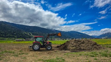 Birgitz, Avusturya - 24 Nisan 2025. Innsbruck yakınlarındaki dağ vadisinde tarım çalışmaları sırasında bir traktör ve gübre yığını. Arka planda Alpler ve gökyüzü var.