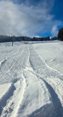 Dağ kayak pistinin görüntüsü, kar kaplı ağaçlara ve dağ manzarasına karşı kayak yamacındaki karı küçültüyor ve düzleştiriyor..