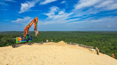 Pyla sur Mer, Fransa - 12 Haziran 2025. Kazıcı Hitachi 'nin çalışması Avrupa' nın en yüksek kum tepesinde, Pilat Kumulunda. Arka planda mavi bir gökyüzü ve yeşil çam ağaçları var..