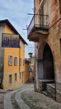 Cannero Riviera, Lago Maggiore, İtalya - 22 Nisan 2023. Eski merkezde dar, dolambaçlı bir kaldırım taşı caddesi. Evlerin arasında bir tablo var..