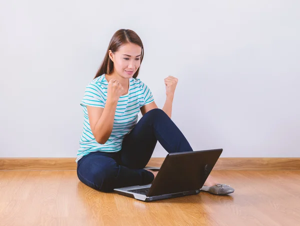 Zittend op de vloer met een laptop die het verhogen van zijn armen met een blik — Stockfoto