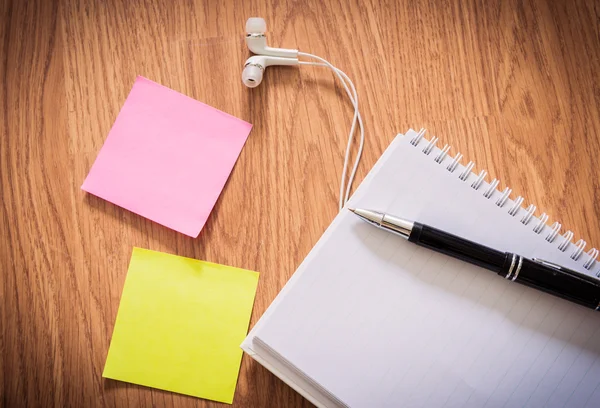 Mesa de oficina con bloc de notas, bolígrafo, auriculares, notas adhesivas — Foto de Stock