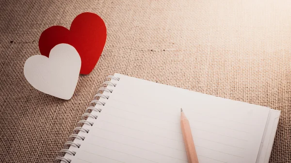 Corazón rojo símbolo y cuaderno en la superficie del saco de tela Imagen de archivo