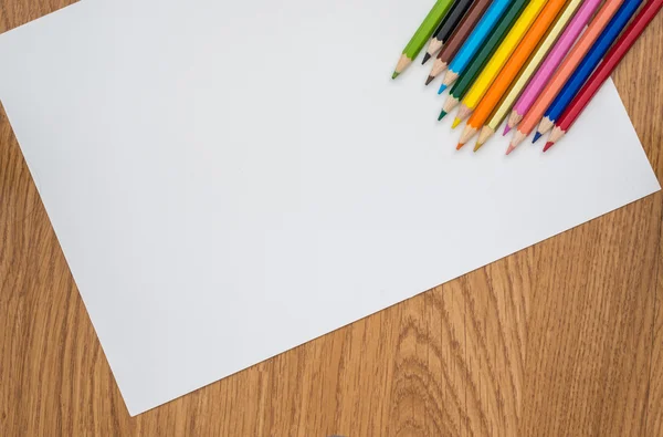 Lápices de color aislados sobre papel blanco y fondo de madera — Foto de Stock