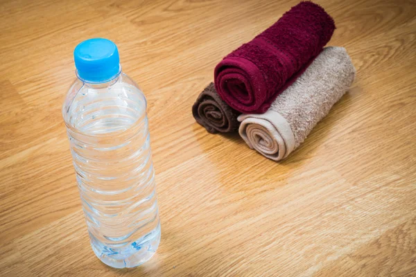 Plastic water bottle and towel on the wooden table — Stock Photo, Image