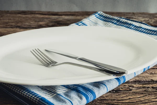 Piatto bianco su un tovagliolo e una forchetta d'argento, coltello. su tavola di legno — Foto Stock