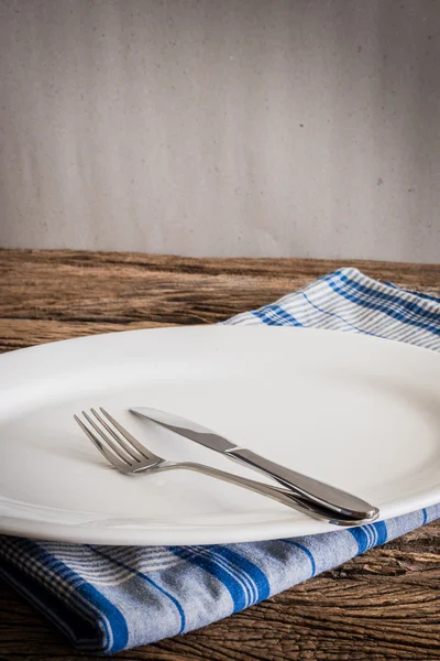 Placa blanca en una servilleta y tenedor de plata, cuchillo. sobre tabla de madera — Foto de Stock