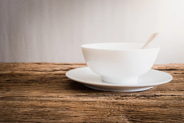 Серебряная ложка в белой миске и белая тарелка на деревянном столе — стоковое фото