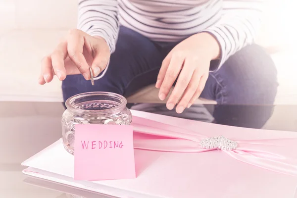 Hand putting a coin into glass jars with 'wedding' text — Stock Photo, Image