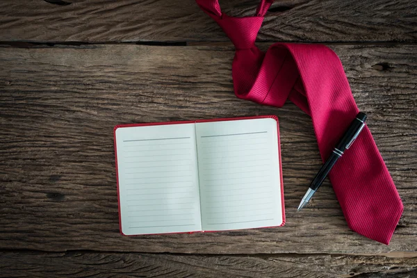 Livre de notes, stylo, cravate rouge sur une surface en bois grunge — Photo