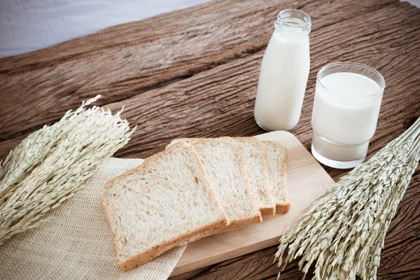 Sklenici mléka a celozrnný chléb na dřevěné desce — Stock fotografie
