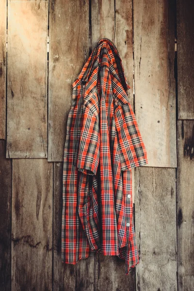 Het oude gerimpelde plaid shirt opknoping op houten achtergrond — Stockfoto