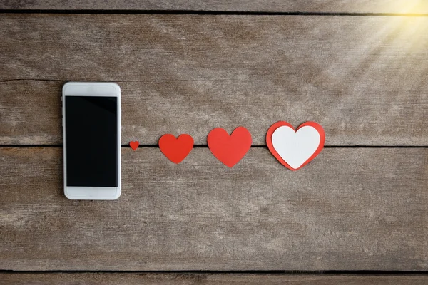 Smartphone y corazones de papel sobre fondo de madera —  Fotos de Stock