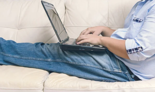 Близко к человеку, работающему с ноутбуком и сидящему на диване — стоковое фото