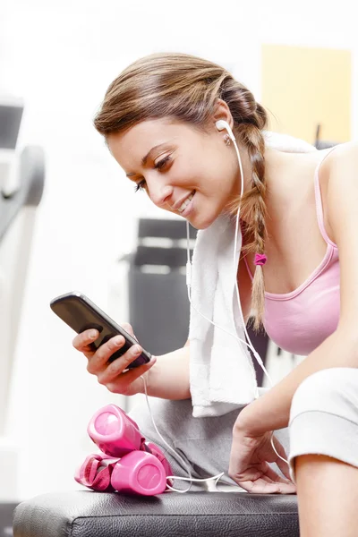 Leende kvinna med smart-telefonen på gymmet — Stockfoto