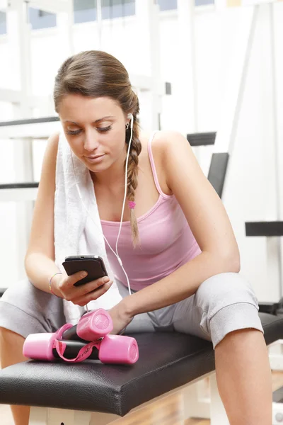 Leende kvinna med smart-telefonen på gymmet — Stockfoto