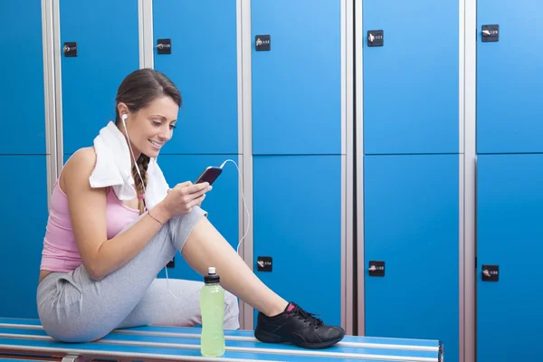 Fitness smiling woman using smart phone in dressing room — Stock Photo, Image