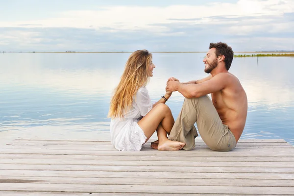 Man and woman couple sitting on a jetty under a blue cloudy sky — Stock Photo, Image