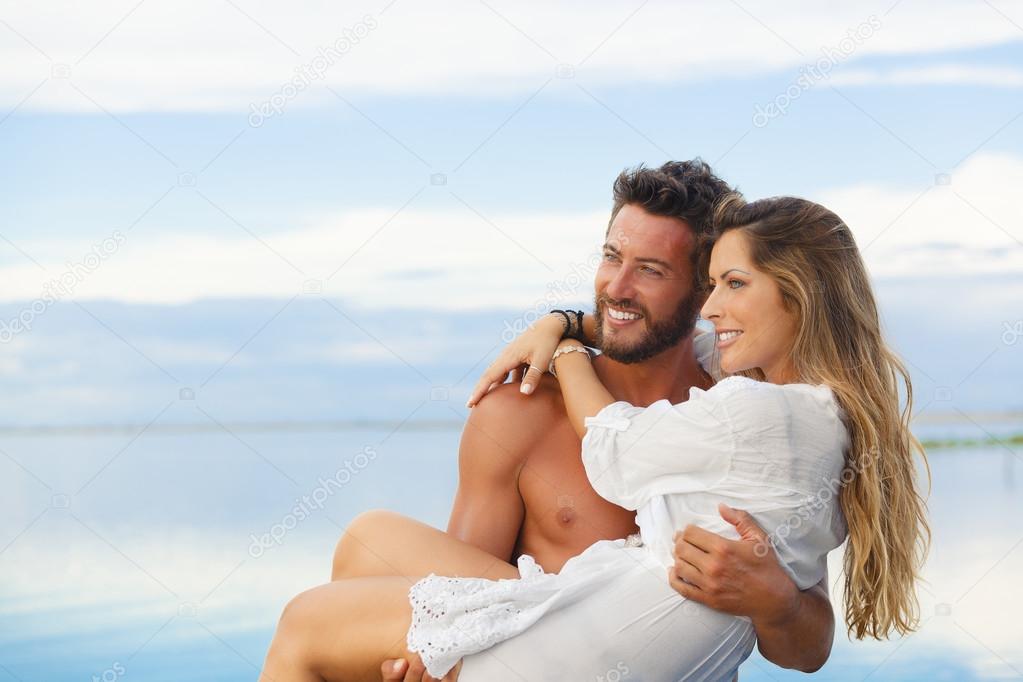Smiling man holding woman in his arms under a blue sky on seasid