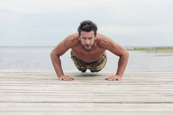 Ejército atlético haciendo ejercicio de empuje hacia arriba en la playa — Foto de Stock