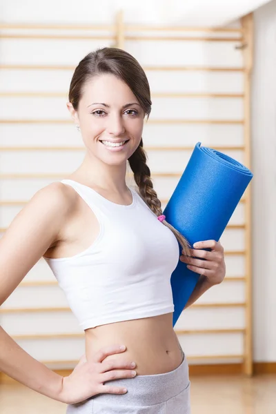 Fitness mladá žena držící modrá Mat v tělocvičně — Stock fotografie