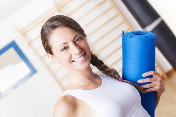 Giovane donna di idoneità che tiene una stuoia blu alla palestra — Foto Stock