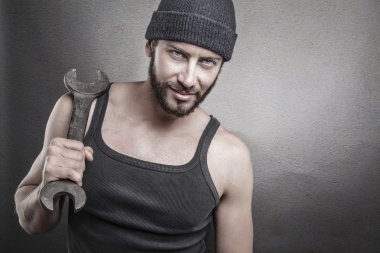 Handsome rough man holding a wrench over a textured grey backgro