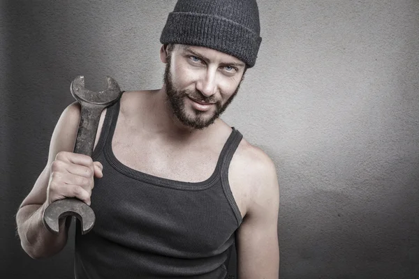 Schöner grober Mann mit einem Schraubenschlüssel über einem strukturierten grauen Backgro — Stockfoto