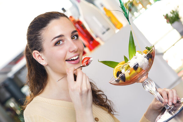 woman eating a strawberry and ice cream dessert in a bar