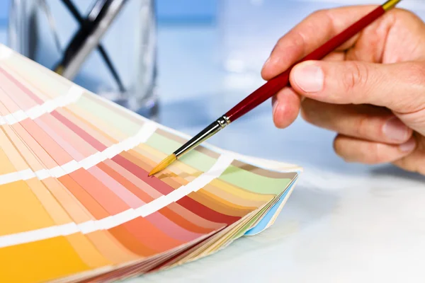 Artist hand pointing to color samples in palette with paintbrush — Stock Photo, Image