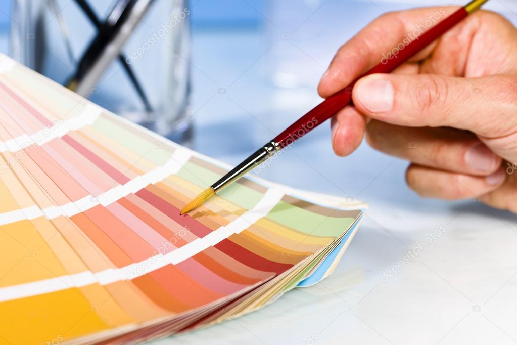 Artist hand pointing to color samples in palette with paintbrush