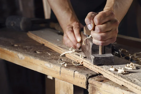 Carpintero cepillando una tabla de madera con un plano de mano —  Fotos de Stock