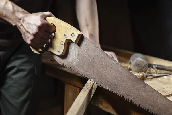 Carpintero aserrando una tabla con una sierra de madera manual —  Fotos de Stock