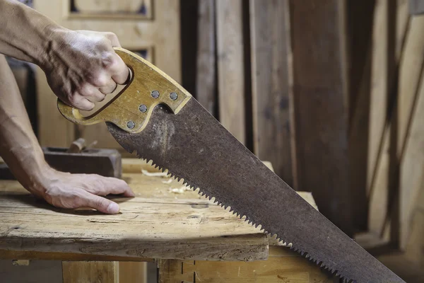 Carpenter sawing a board with a hand wood saw