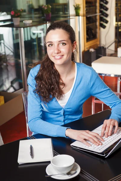 Chica sonriente tomando un descanso para tomar café y trabajando en una computadora —  Fotos de Stock