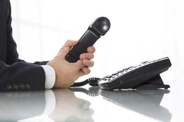 Businessman holding the receiver of a black landline telephone Stock Picture