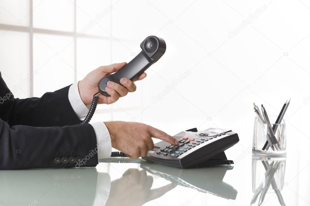 Businessman hands dialing out on a black deskphone