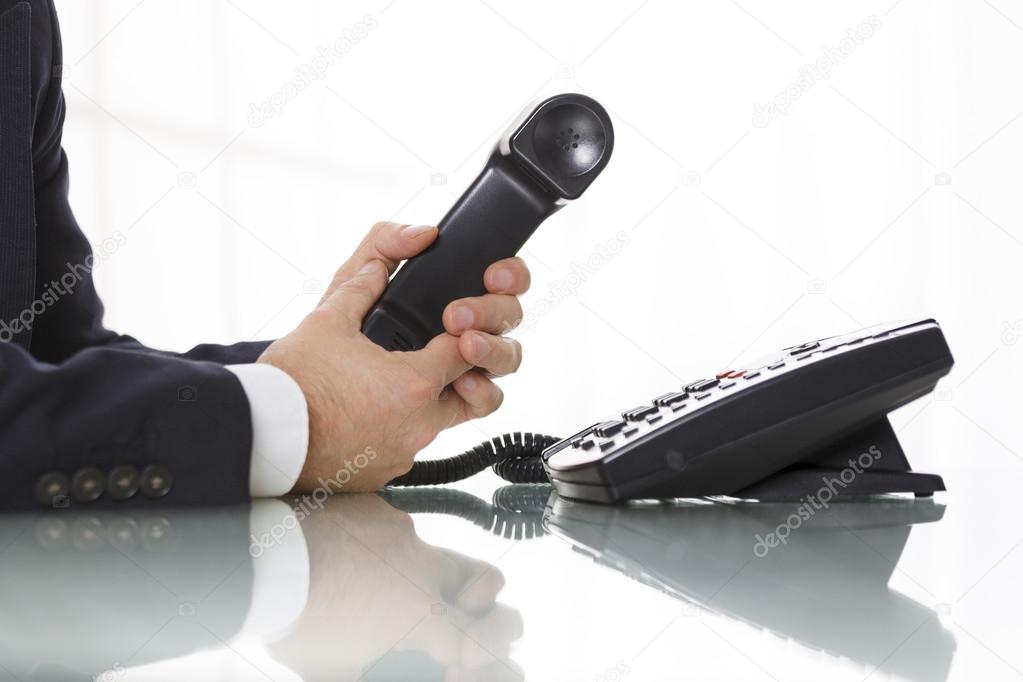 Businessman holding the receiver of a black landline telephone