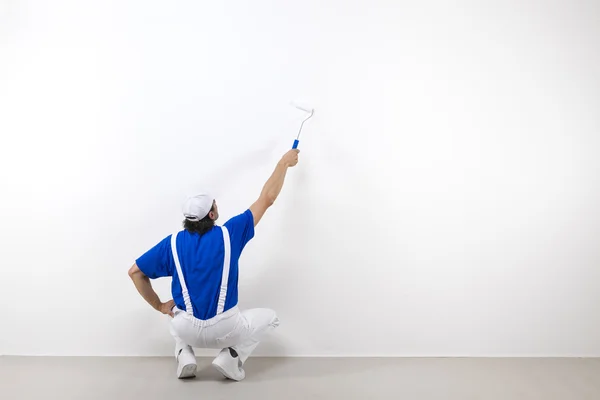 Hukande målare med paintroller på vit vägg — Stockfoto