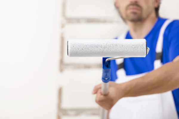 Close up shot of painter man aiming at you with paint roller. — Stock Photo, Image