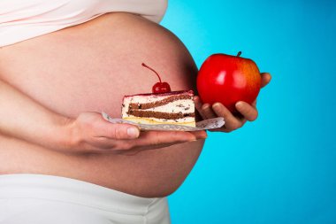 Bir apple ve mavi zemin üzerine pasta dilimi ile hamile kadın