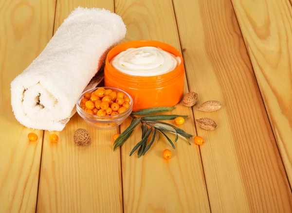 Towel, sea buckthorn and cream out of it against the backdrop  pale wood — Stock Photo, Image