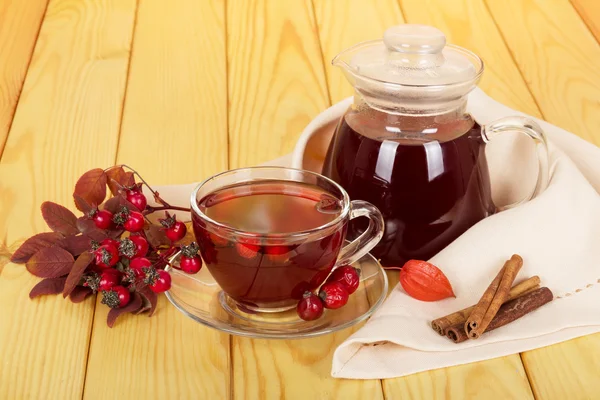 Caraffa e tazza di bevanda rosa canina, bastoncini di vaniglia su uno sfondo di legno chiaro . — Foto Stock