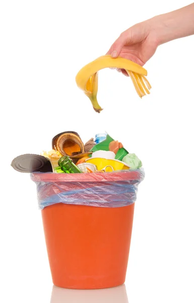 A mão feminina coloca uma casca de banana no balde de lixo doméstico isolado no fundo branco . — Fotografia de Stock