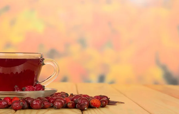 Cup with  drink from  dog rose berries on  autumn leaves. — Stock Photo, Image