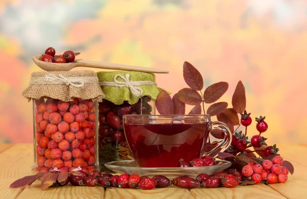 In glass jars rosehip berries, mountain ash and  cup tea. — Stock Photo, Image