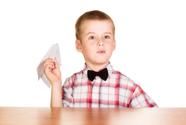 Niño se sienta a la mesa y sostiene avión de papel aislado . —  Fotos de Stock