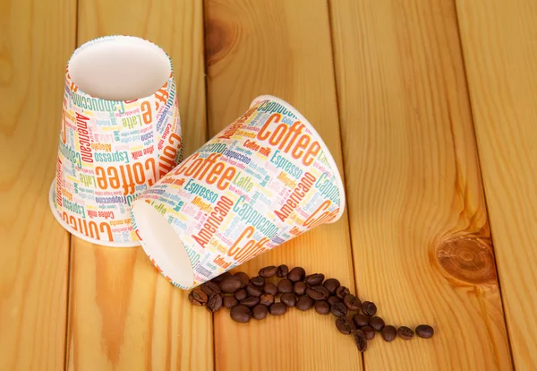 Tasses en papier vides et grains de café sur fond bois clair . — Photo