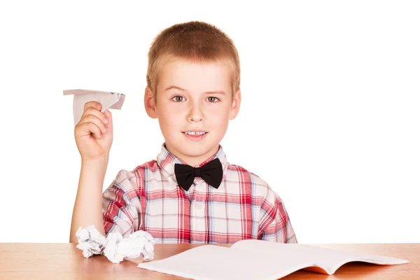 Chłopiec siedzi na stół i zrobić papierowe samoloty na białym tle. — Zdjęcie stockowe